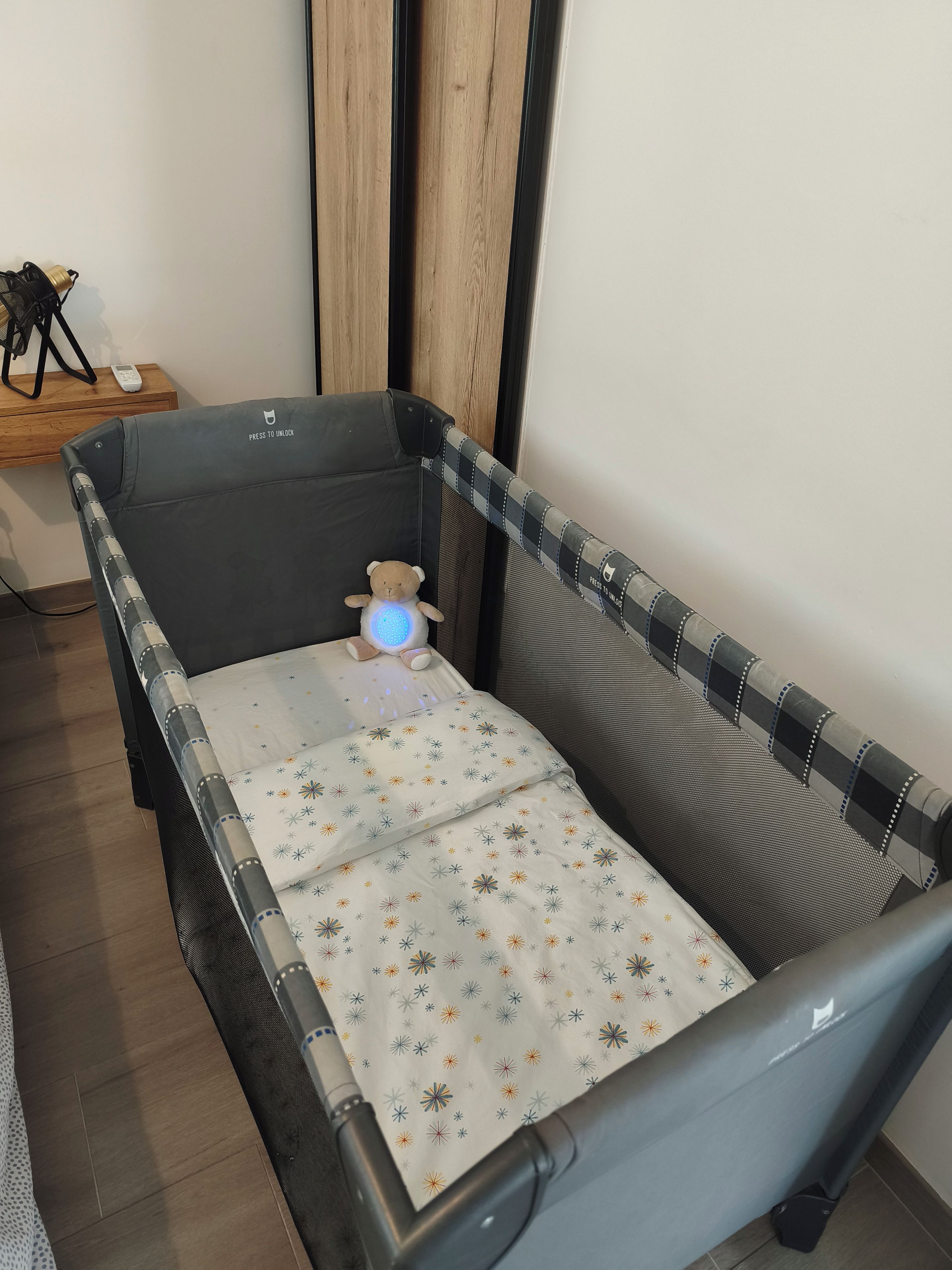 Ein Babybett mit einem gemusterten Matratze, einem Teddybären und einer Babywiege mit blauem Licht.