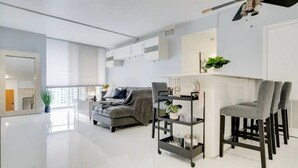 A modern living room with a grey sofa, a black metal shelf with decorative items, and a grey chair. - Chic Penthouse: 3BR | Pool | Gym| 2 Parking Spots (Miami)