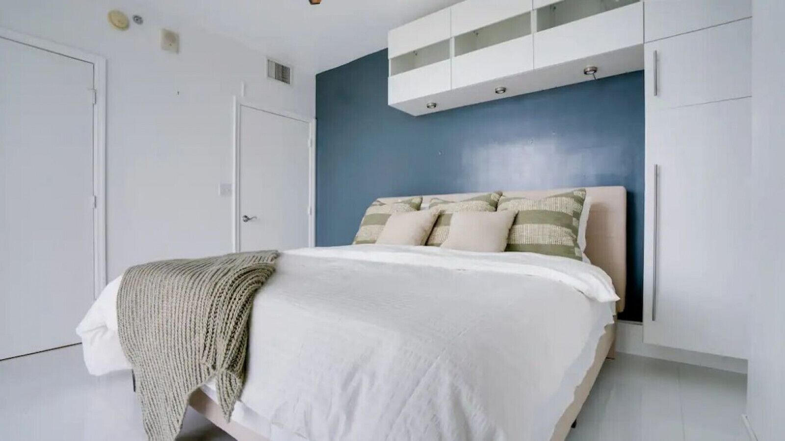 A bedroom with a bed, white walls, a blue accent wall, and built-in white cabinets.