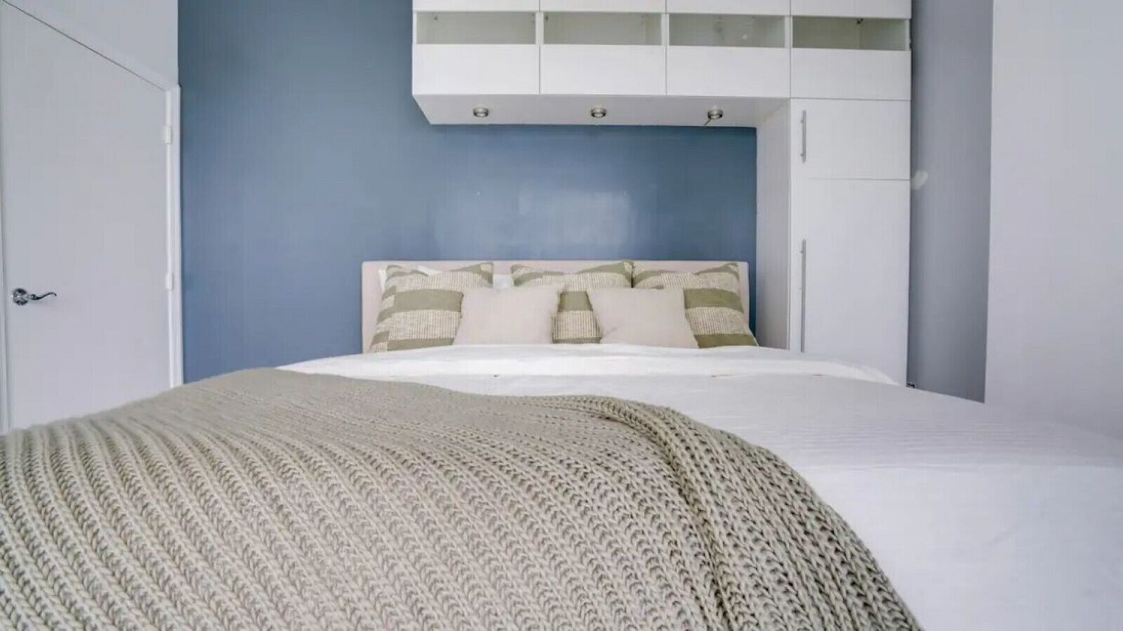 A bedroom with a bed, a white wardrobe, and a blue wall.