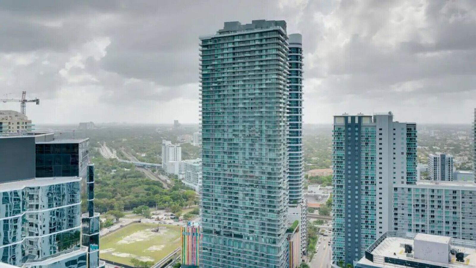 Un edifici alt amb façana de vidre modern, envoltat d'altres edificis alts i una vista llunyana d'un paisatge urbà.