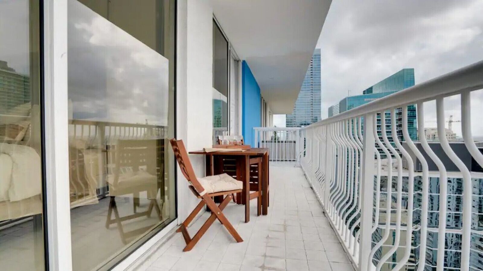 Un balcón con mesa y sillas, un ventanal de vidrio y vista a la ciudad.