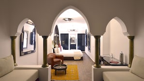 A hotel room with a bed, a sofa, a small table with a vase, and a yellow rug. - Riad Spa Le Secret de Zoraida (Marrakech)