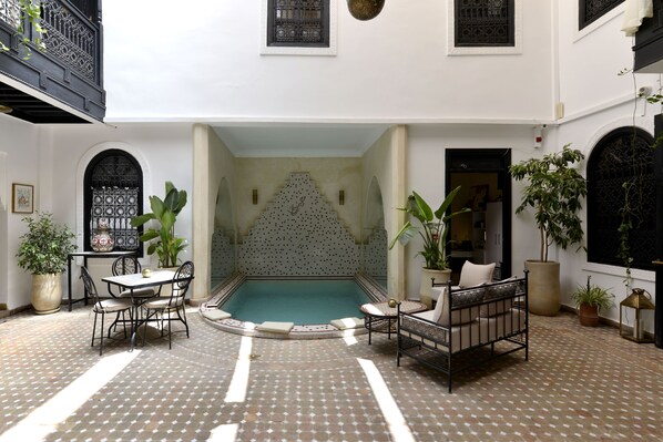 Un patio con piscina, zona de estar y plantas en macetas.