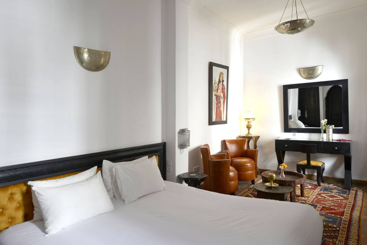 A hotel room with a bed, a desk, a chair, a lamp, and a mirror.