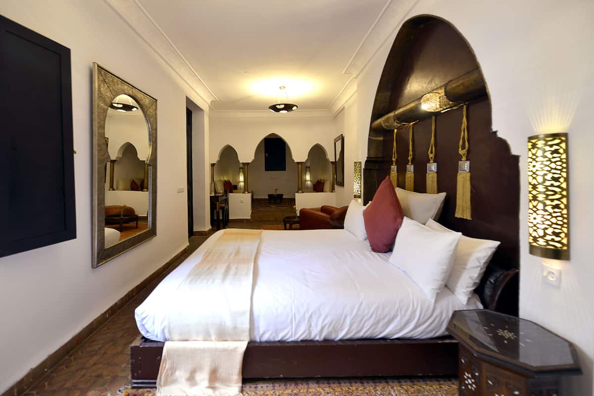 A hotel room with a large bed, a sitting area with a chair, a desk, and a mirror.
