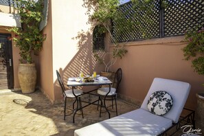A patio with a table set for breakfast, two chairs, and a lounge chair with a patterned cushion. - Riad Spa Le Secret de Zoraida (Marrakech)