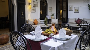 A dining area with a table set for two, featuring plates, cutlery, and a bowl of food. There are chairs around the table, and a sofa with cushions in the background. - Riad Spa Le Secret de Zoraida (Marrakech)