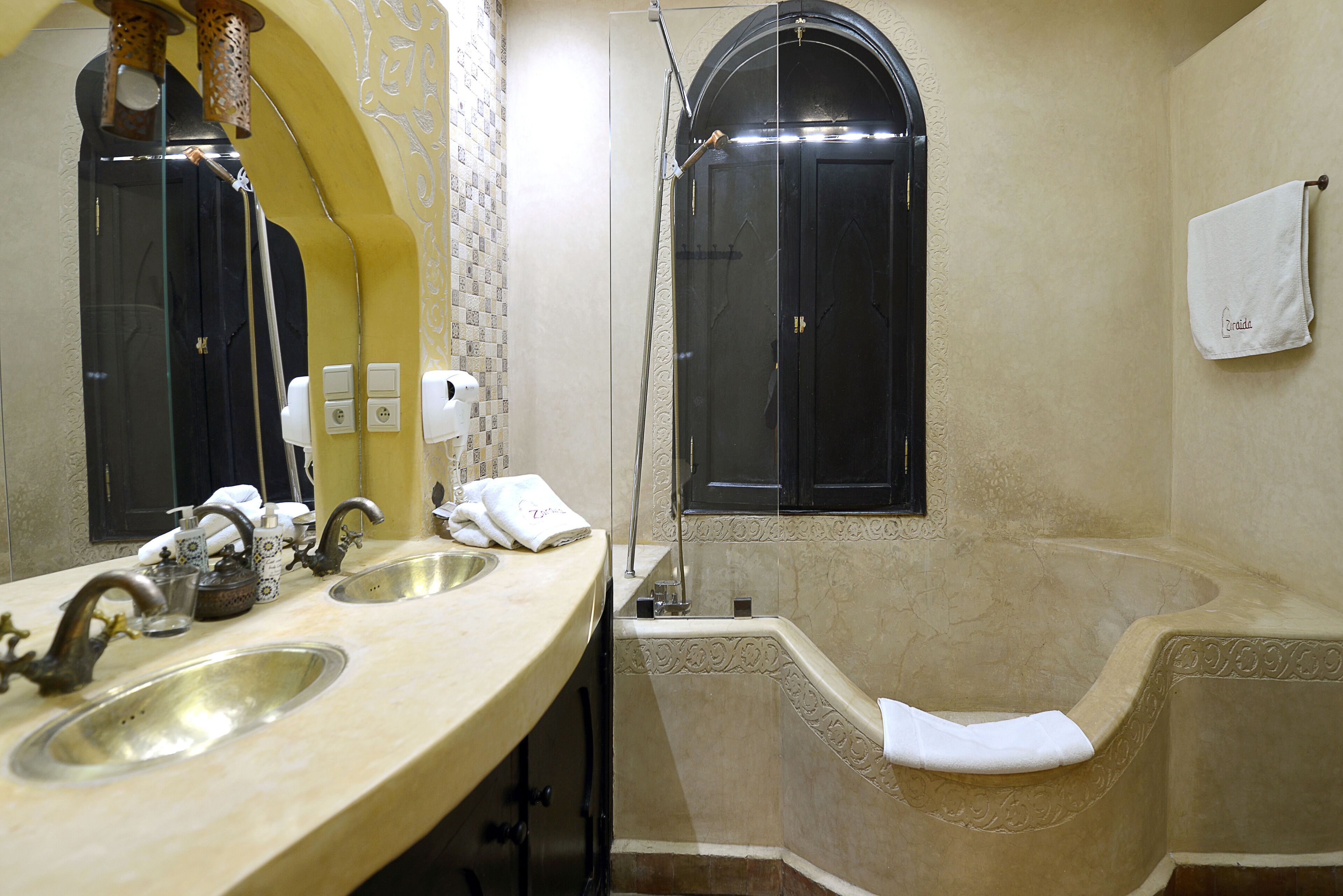 A bathroom with two sinks, a large mirror, a shower, and a towel hanging on the wall.