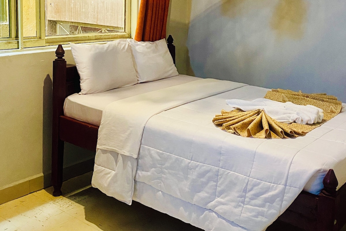 A neatly made bed with white linens, a wooden headboard, and a window with curtains.