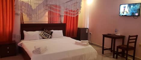 A neatly made bed with a white comforter and pillows, a small table with a chair, and a television mounted on the wall.