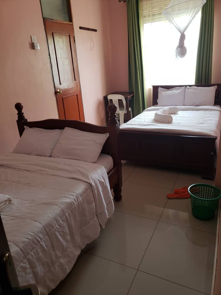 A room with two beds, a chair, a green basket, and a door.