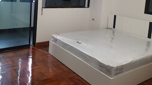 Ein Zimmer mit Holzboden, einem Bett, einem Fenster und einer Klimaanlage.