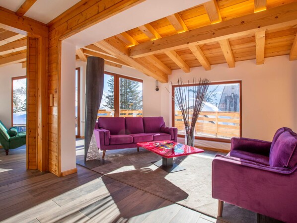 Un espacio habitable espacioso con techo de madera, ventanas amplias que ofrecen vista al exterior, un sofá púrpura y una mesa de centro.