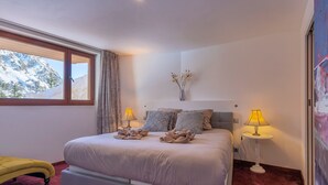 Una camera da letto con un letto, due lampade sui comodini, una finestra con tende, un vaso con rami e un quadro appeso al muro.