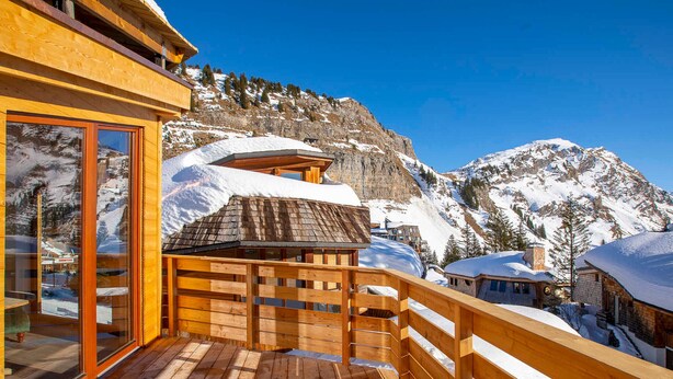 Un terrazzo in legno con struttura in vetro che si affaccia su un paesaggio montano innevato.