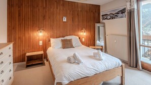 A bedroom with a wooden headboard, a bed with white linens, two bedside lamps, a dresser, and a large window with a view of a mountainous landscape. - 3-room apartment 5 min from Morzine center (Morzine)