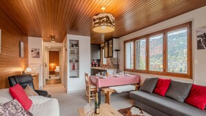 A cozy living room with a wooden ceiling, a dining area with a checkered tablecloth, and a sofa with red cushions. - 3-room apartment 5 min from Morzine center (Morzine)