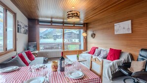 A cozy dining area with a checkered tablecloth, wooden ceiling, and a view of mountains through large windows. - 3-room apartment 5 min from Morzine center (Morzine)