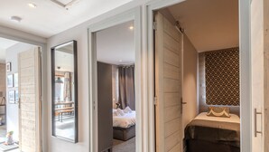 A hotel room with a bed, a small seating area, a bathroom with a patterned shower curtain, and a hallway leading to another room. - Renovated 3-room apartment in Morzine, near center, includes WiFi (Morzine)