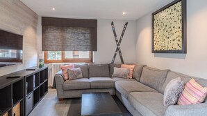A modern living room with a sectional sofa, a flat-screen TV, a coffee table, and a large abstract painting on the wall. - Renovated 3-room apartment in Morzine, near center, includes WiFi (Morzine)