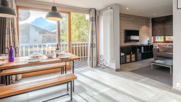A spacious living area with a dining table, benches, a sofa, and a TV. - Renovated 3-room apartment in Morzine, near center, includes WiFi (Morzine)
