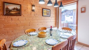A wooden interior with a dining table set for four, surrounded by wooden chairs. There are hanging pendant lights above the table, and a window providing a view outside. - Comfortable 4-room in Morzine, terrace, garage, near center (Morzine)