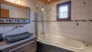 Ett modernt badrum med ett fristående badkar, en stor spegel och ett fönster med utsikt över omgivningen.