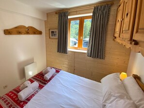 A wooden cabin room with a bed, a window with curtains, and a wooden headboard.