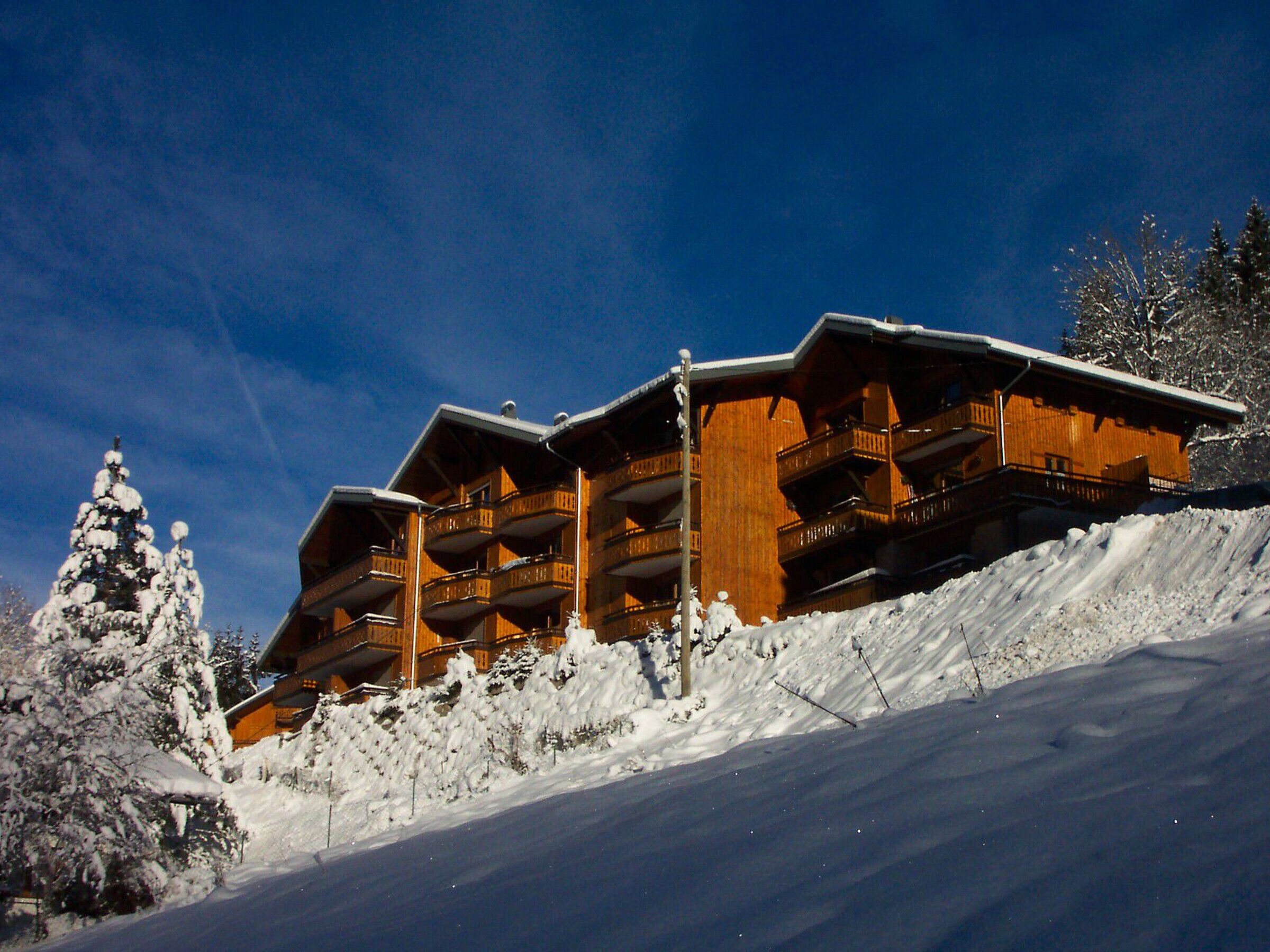 A wooden chalet with multiple balconies, situated on a snow-covered slope.