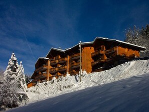 Een houten chalet met meerdere balkons, gelegen op een met sneeuw bedekte helling.