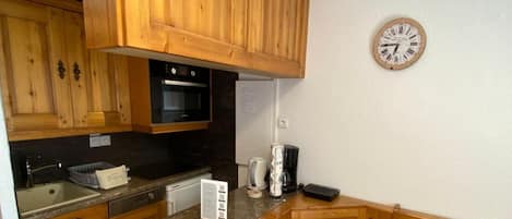 Una cocina con armarios de madera, un microondas, una cafetera y un reloj en la pared.