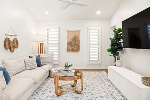 A modern living room with a sofa, a round wooden coffee table, and a TV mounted on the wall.