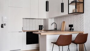 A modern kitchen with a built-in dishwasher, a wooden countertop, a black coffee maker, and two bar stools.