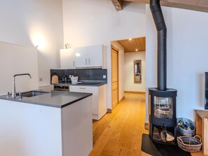 Een moderne keuken met een centraal eiland, witte kasten en een houtkachel.
