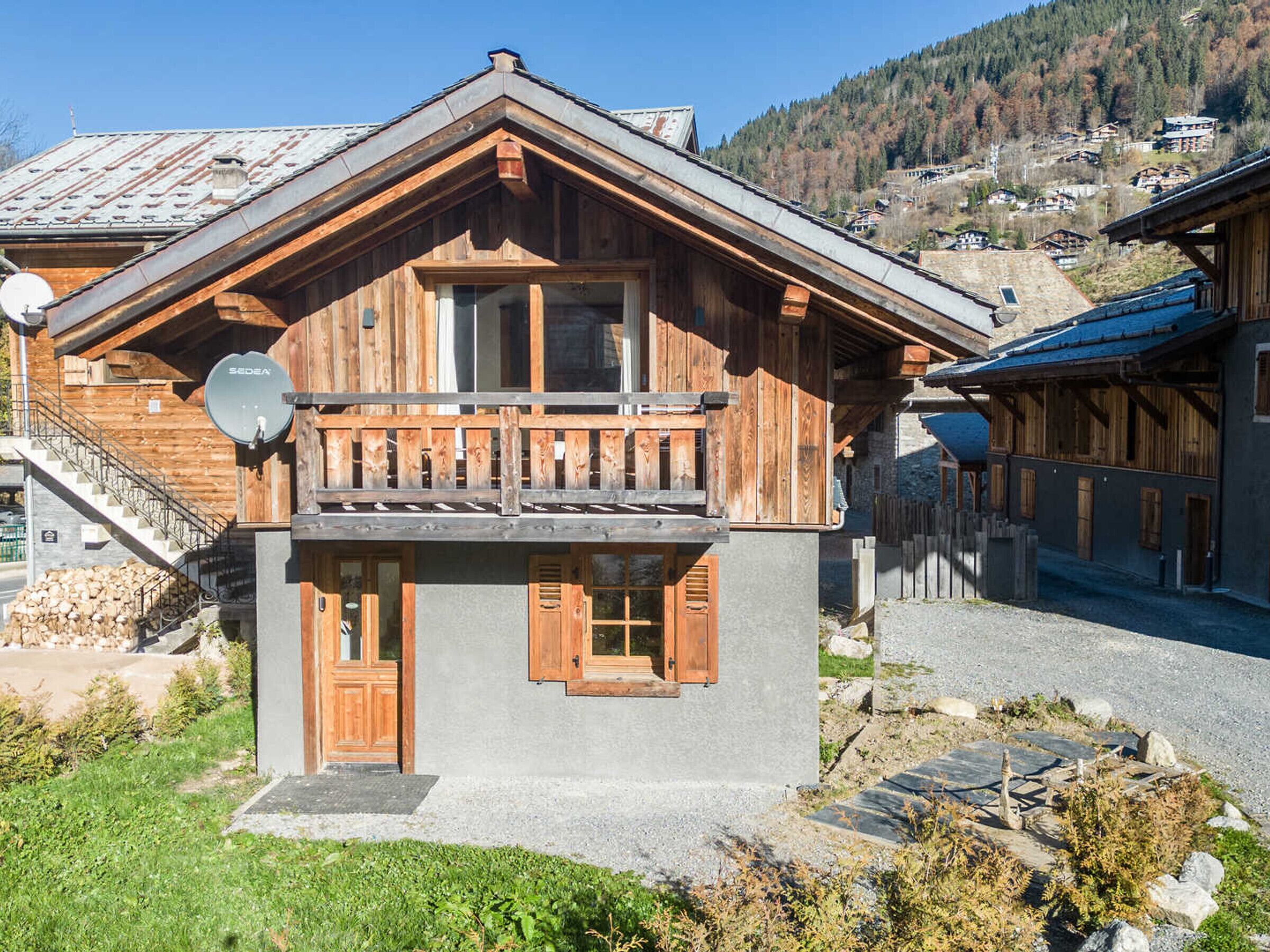 Un chalet de madera con balcón, antena parabólica y una escalera de piedra que lleva a un nivel superior.