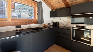 A modern kitchen with a built-in oven, a sink, and a window offering a view of a mountainous landscape. - Charming renovated chalet in Morzine center with parking, sleeps 4. (Morzine)