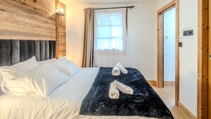 A bedroom with a wooden headboard, a bed with white linens, a black velvet bedspread, and two rolled towels. - Charming renovated chalet in Morzine center with parking, sleeps 4. (Morzine)