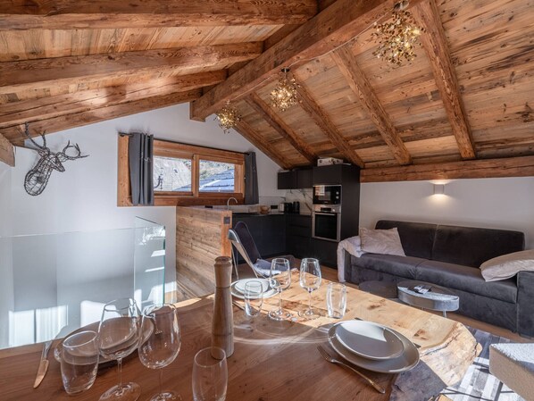 A cozy wooden interior with a dining table set for six, a sofa, and a kitchen area.