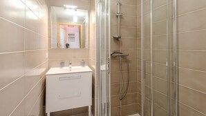 A modern bathroom with a glass-enclosed shower, a white vanity with a mirror, and beige tiled walls.
