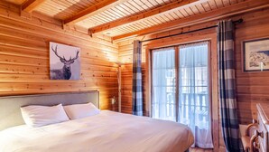 A wooden cabin bedroom with a bed, a framed deer picture, and a window with curtains.