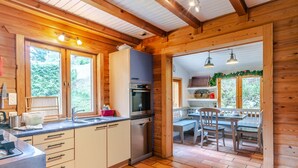 A wooden cabin kitchen with a built-in oven, a sink, and a dining area with a table and chairs.