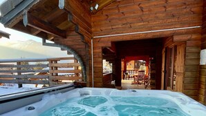 A wooden cabin with a hot tub and a view of the mountains.