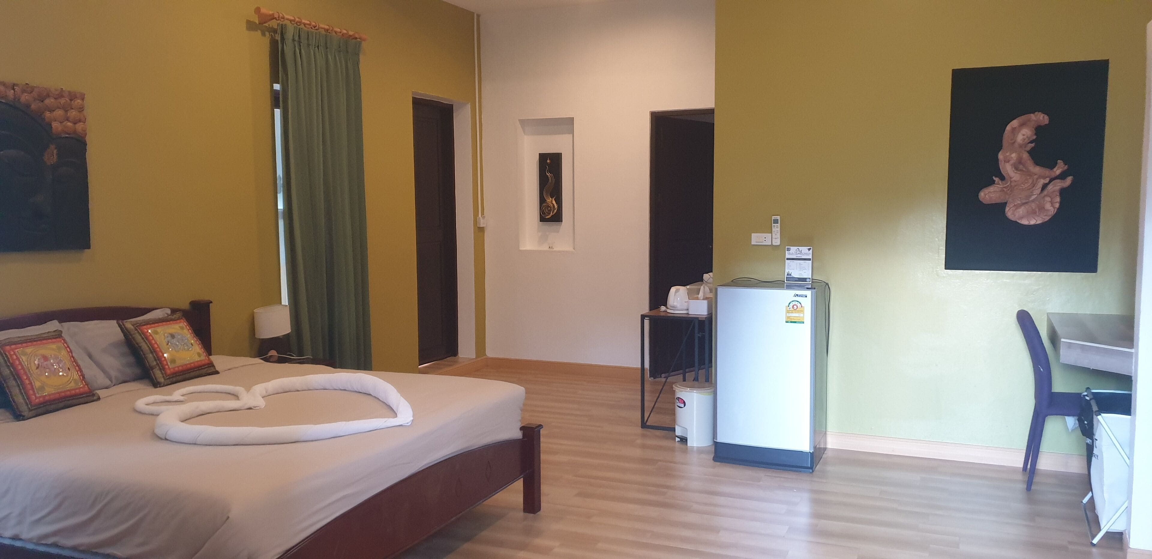 Ett hotellrum med en säng, ett skrivbord, en stol, ett kylskåp och en papperskorg.