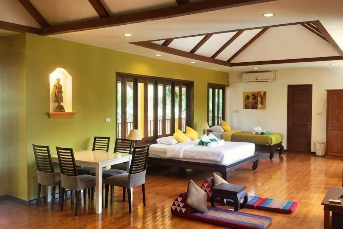 A room with a bed, a dining table with chairs, a sofa, and a small table with a lamp.
