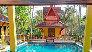 Une piscine bordée de carreaux, un petit jacuzzi et un pavillon surmonté d’un toit rouge.