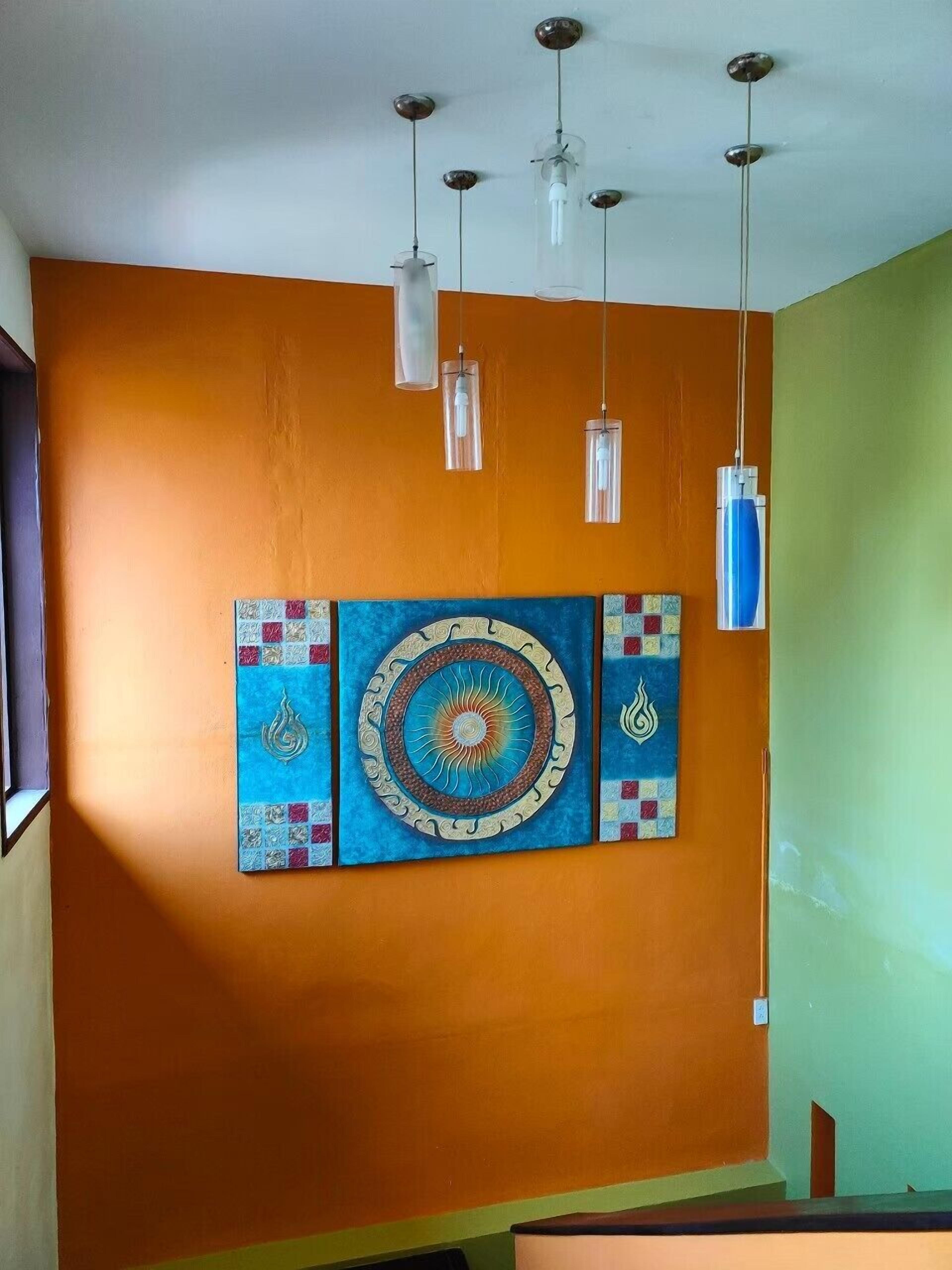 Une pièce aux murs orange, ornée d’une œuvre d’art aux couleurs bleu et or, et éclairée par trois suspensions.