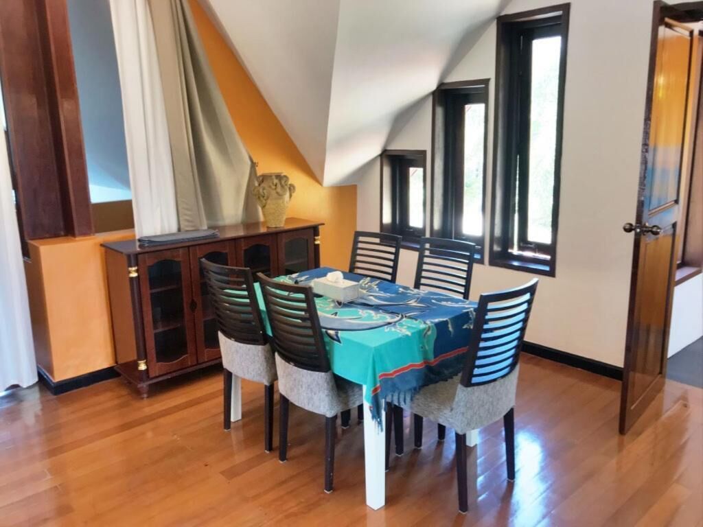 A dining area with a table set for six, wooden chairs, a cabinet with glass doors, and a view of the outdoors through windows.
