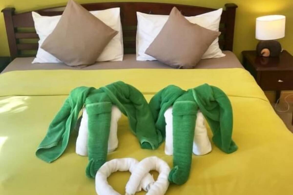 A bed with a green blanket and a heart-shaped towel arrangement.