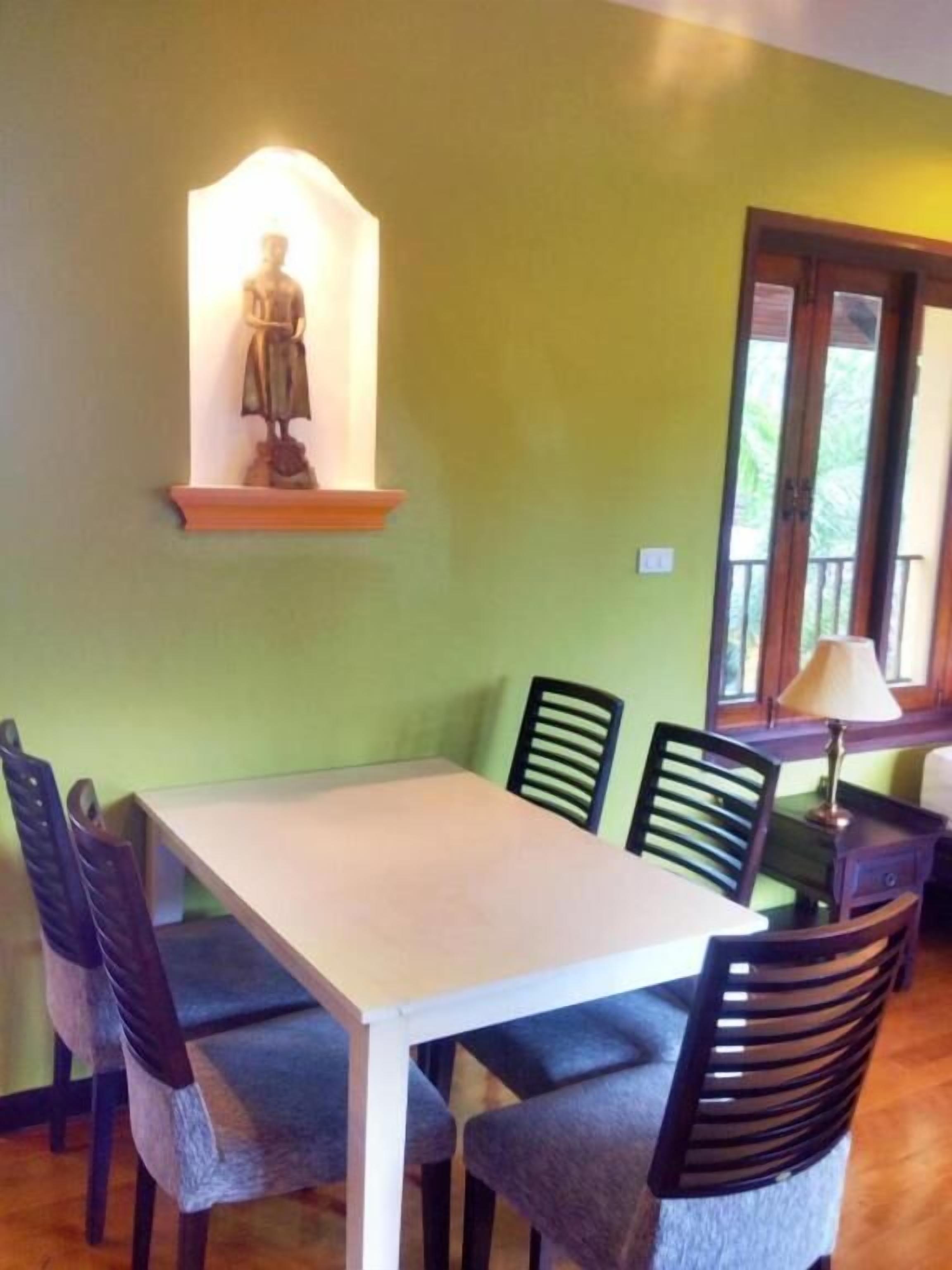 A dining area with a table and chairs, a statue on a shelf, and a window with a view of greenery.